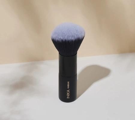 INIKA Organic Kabuki brush standing upright on a light background with a black handle and dense rounded bristles fading to lighter tips.