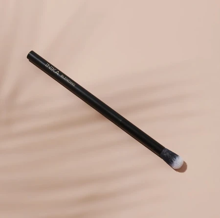 INIKA Organic Blending Brush on a beige background, with a slim black handle and rounded soft bristles in white and black tones.