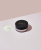 Round INIKA container with a black lid and a small amount of loose light powder beside it on a pale pink background.