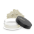 Partly open clear jar with a matte black INIKA lid and loose light powder scattered beside it.