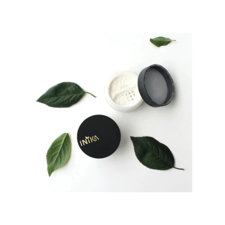 Open INIKA container with loose white powder, black lid with gold INIKA logo and green leaves on a white background.