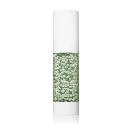 Elegant white airless pump serum bottle with green active-ingredient capsules suspended in a gel base.