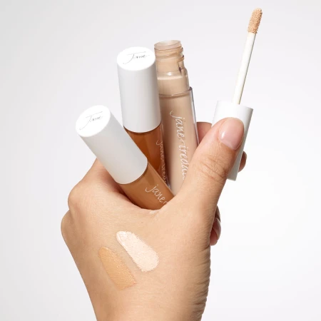 Hand holding three PureMatch Liquid Concealers with applicator and shade swatches on the skin.