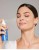Woman misting her face with Jane Iredale D₂O Hydration Spray from a blue bottle, ideal for dry skin.