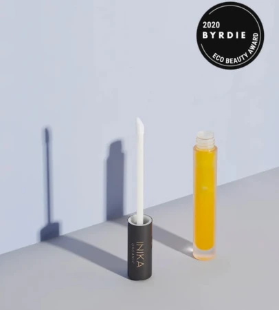 INIKA Organic Lip Serum in a glass bottle with yellow liquid and applicator beside it, with 2020 Byrdie Eco Beauty Award badge.