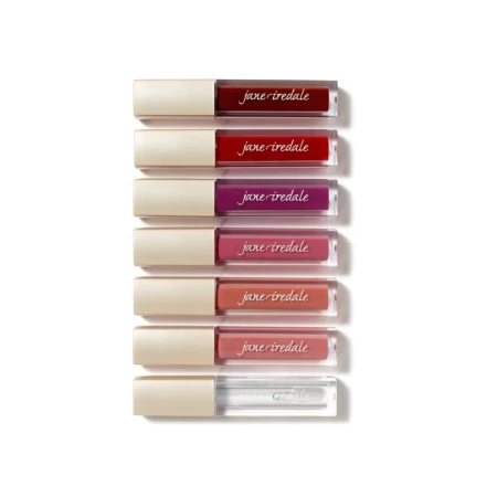 Na zdjęciu znajduje się zestaw błyszczyków marki Jane Iredale. Produkty ułożone są pionowo, jeden nad drugim, w eleganckich opakowaniach z beżową nakrętką i przezroczystym korpusem, przez który widać kolor błyszczyka.