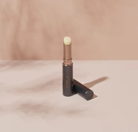 INIKA Organic Lip Balm standing upright on an elegant beige and pink background.