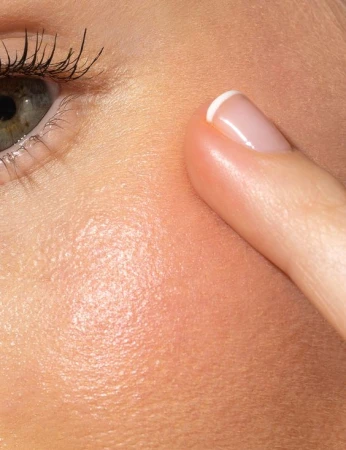 Close-up of cheek skin with product gently applied by fingertip, giving a hydrated luminous glow.