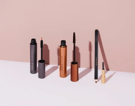 Four INIKA Organic eye makeup products displayed on a pale pink background.