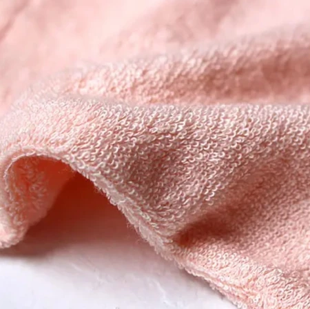 Soft pale pink Jane Iredale Magic Mitt makeup remover mitt with brand tag.