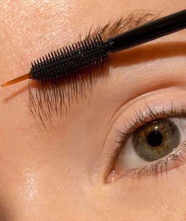 Close-up of an eyebrow being brushed with INIKA Organic Lash & Brow Serum using a black spoolie applicator.