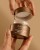 Hands opening the metallic bronze INIKA Organic Overnight Repair Treatment jar and revealing the inner lid.