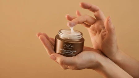 Hands holding INIKA Organic Overnight Repair Treatment and taking a small amount of the silky cream formula.
