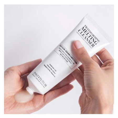 Hands squeezing INSTYTUTUM Transforming Melting Cleanser from a white tube onto the palm.