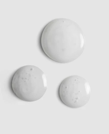 Close-up of three slightly milky gel droplets on a smooth grey background.