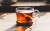 Clear glass of amber rooibos tea on a wooden saucer with a tea bag and visible steam.