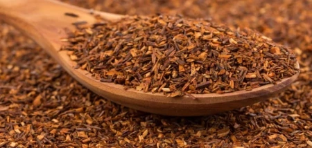 Wooden spoon filled with finely cut dried rooibos leaves on a natural rooibos background.