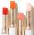 Four Jane Iredale Just Kissed Lip and Cheek Stain balms in different shades, shown in elegant white and gold packaging.