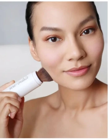 Woman applying Jane Iredale Powder-Me SPF powder sunscreen with the brush outdoors on a sunny day.