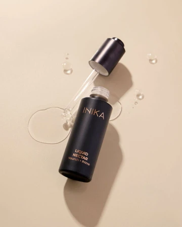 Open INIKA Organic Liquid Nectar Nourish + Prime bottle lying on a light surface beside the dropper cap.