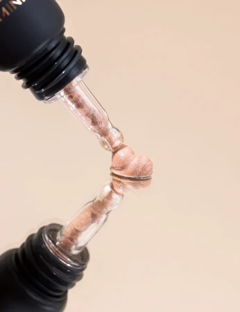Pink-gold cream highlighter texture from INIKA Organic Cream Illuminisor PINK PEARL on a clear applicator tip.