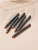 Six INIKA Organic Lip Crayons arranged diagonally on a warm nude background with a soft palm-leaf shadow.