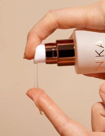 Clear INIKA Organic Adaptogenic Cleansing Oil texture flowing onto fingertips during application.