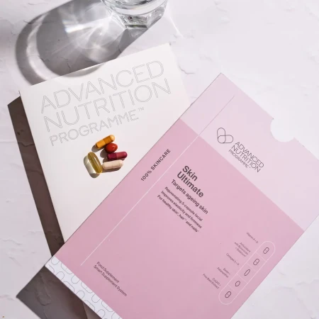 Advanced Nutrition Programme Skin Ultimate supplement set with pink packaging, capsules, folder and glass of water.