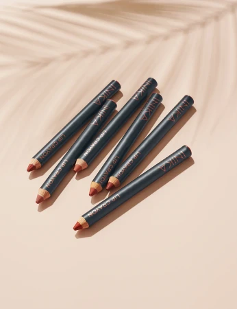 Six INIKA Organic Lip Crayons on a light background with a soft natural leaf shadow.