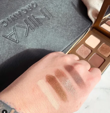 Swatches of four INIKA Organic Quad Eyeshadow Palette WIND shades on a hand beside the open palette.