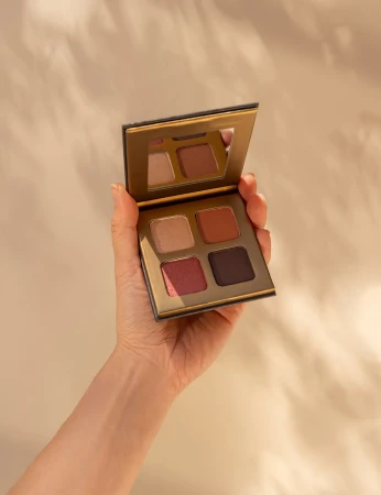 Open INIKA Organic Quad Eyeshadow Palette FLOWERS held in a hand with beige, brick, burgundy and brown shades.