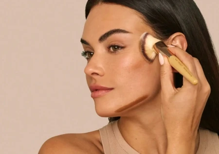Model applying cream bronzer under the cheekbone for soft contour.