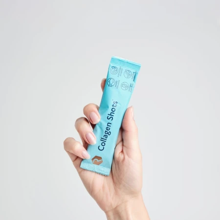 Hand holding a single light blue Rejuvenated Collagen Shots sachet.