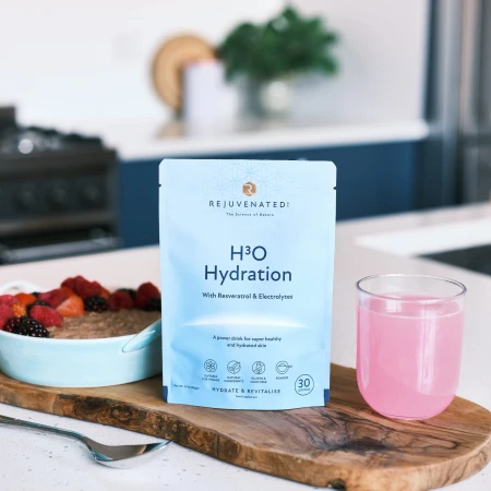 REJUVENATED H3O Hydration Powder sachet next to a glass of prepared pink drink on a tabletop