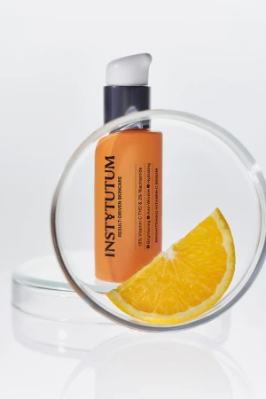 INSTYTUTUM Brightening Vitamin C Serum orange pump bottle shown with a piece of orange.