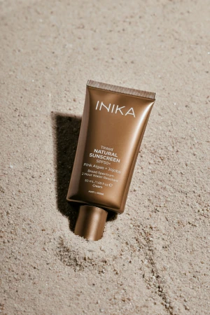 INIKA Tinted Natural Sunscreen SPF50+ tube on light sand
