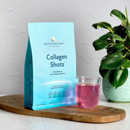 Rejuvenated Collagen Shots pouch with a glass of pink drink on a wooden board