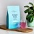 Rejuvenated Collagen Shots pouch with a glass of pink drink on a wooden board