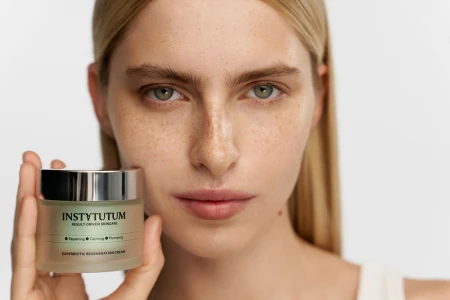 Model holding INSTYTUTUM SuperBiotic Regenerating Cream jar, highlighting smooth radiant-looking skin.