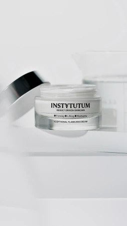 Open jar of INSTYTUTUM Xceptional Flawless Cream with silver lid on a light background