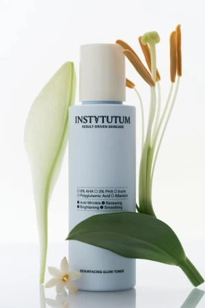 INSTYTUTUM Resurfacing Glow Toner bottle among green leaves and flowers
